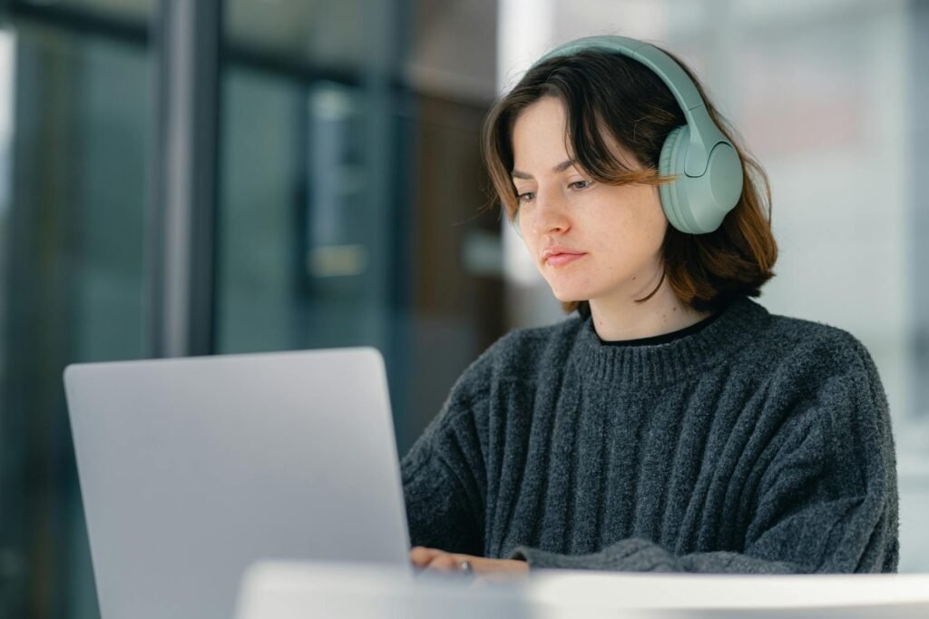 Young woman wearing headphones working on a laptop indoors, focused and engaged.