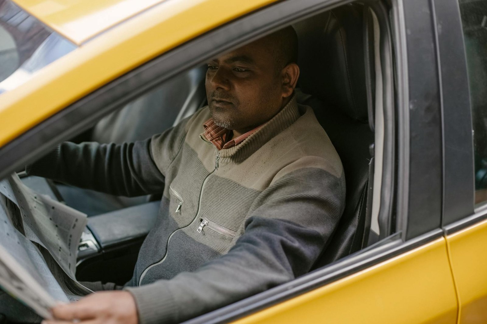 Ethnic male driver reading daily newspaper with interest while sitting in car and having break