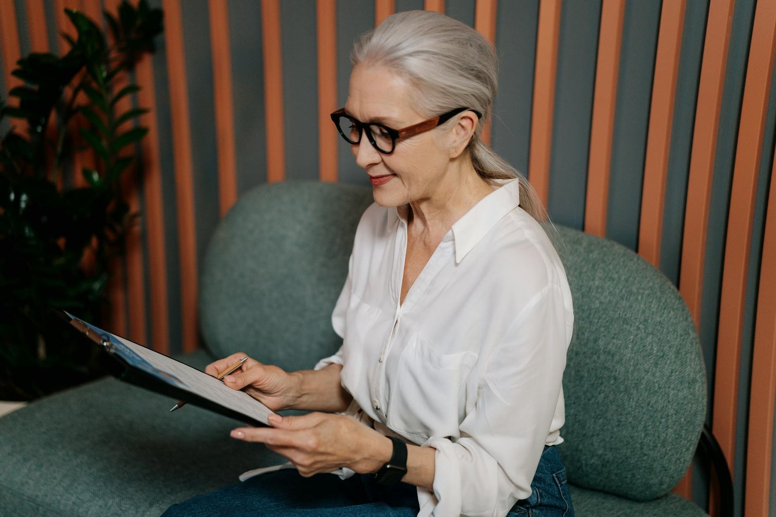 image Woman in White Dress Shirt and Black Pants Wearing Black Framed Eyeglasses Sitting on Gray Couch
