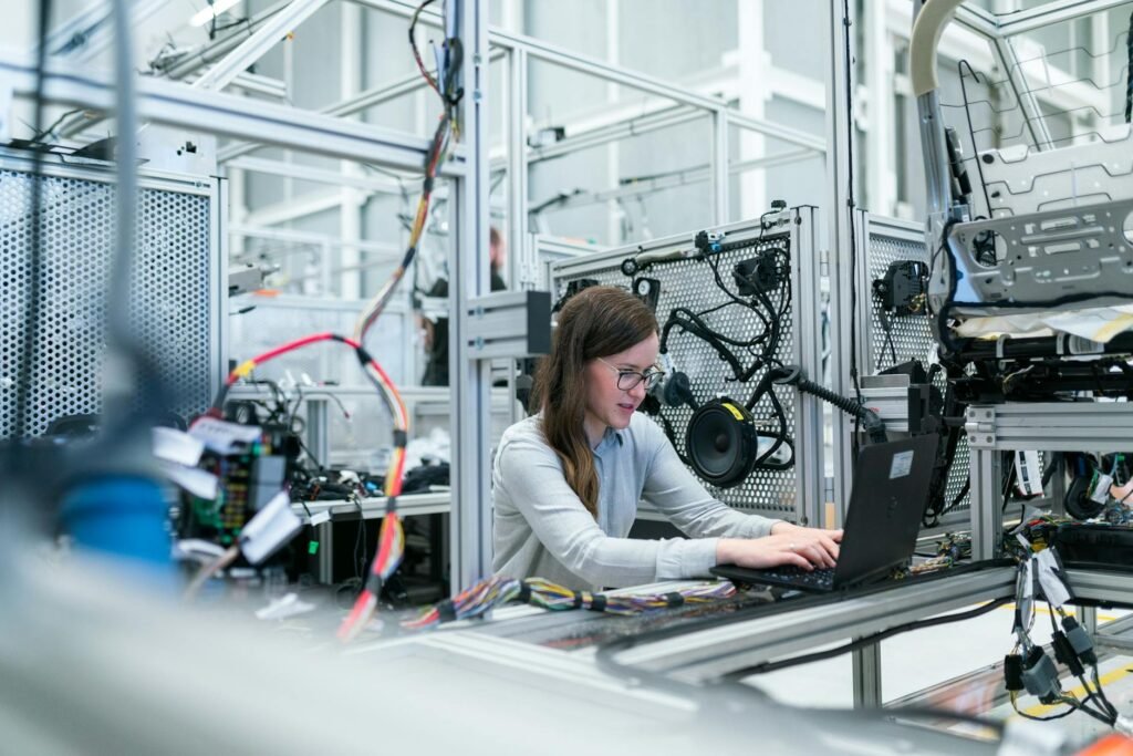 A female engineer focuses on her laptop amidst advanced tech equipment in a lab.