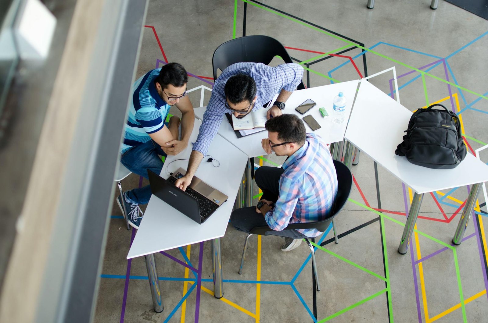 image Three men collaborating over a laptop in a modern, geometric-themed office space.