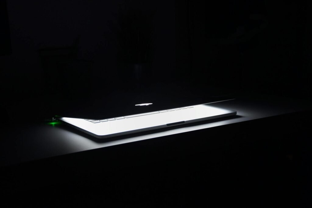 A dramatic, low-light image of a slightly open laptop with glowing keys on a dark desk.